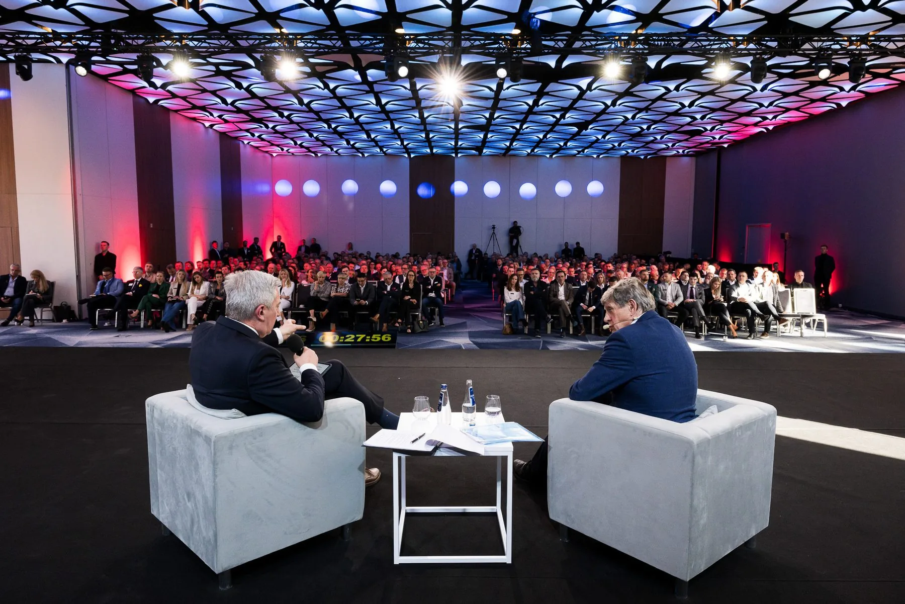 Sala Business Weekend The Company: rozmowa dwóch prowadzących na scenie, publiczność pod dekoracyjnym sufitem.