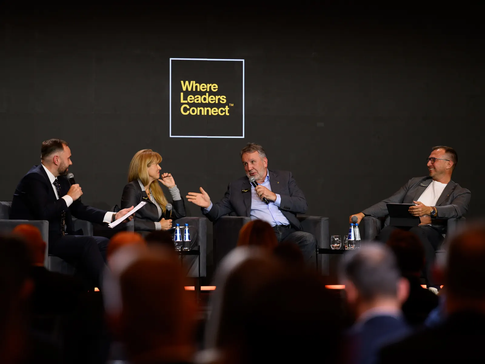 Panel na scenie: czworo rozmówców w fotelach przed pełną salą, w tle znaki Corporate Connections i the company oraz tablica Where Leaders Connect.