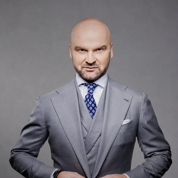 Rafał Brzoska w szarym trzyczęściowym garniturze i granatowym krawacie, portret na szarym tle.