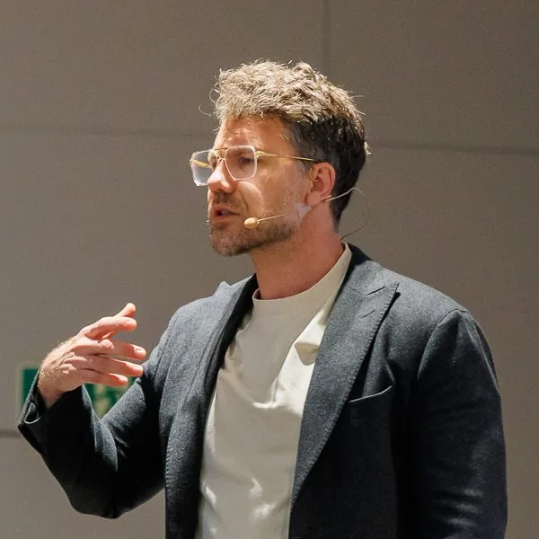 dr Mateusz Grzesiak podczas wystąpienia, w mikrofonie nagłownym, w trakcie gestu.