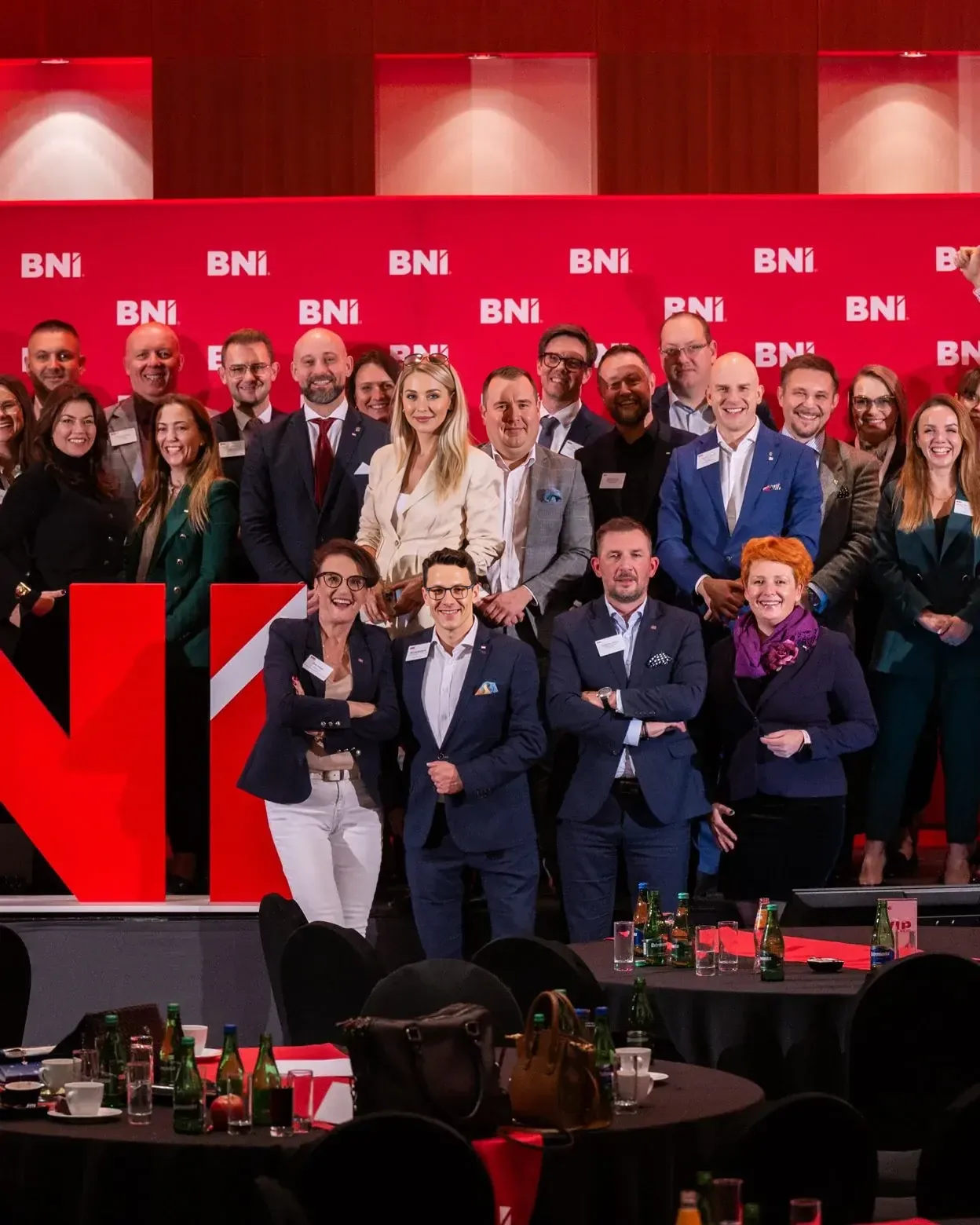 Kilkadziesiąt przedsiębiorczyń i przedsiębiorców pozuje razem na scenie przed ścianką z logotypami BNI.